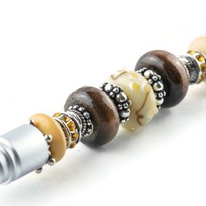 May include: A silver stylus pen with brown, white, and gold beads. The beads are decorated with silver accents.