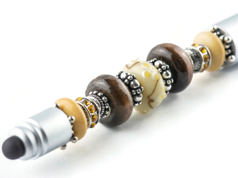 May include: A silver stylus pen with brown, white, and gold beads. The beads are decorated with silver accents.