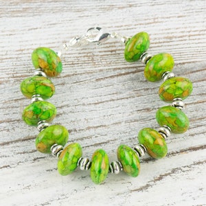 Pode incluir: Um bracelete de pedra verde e marrom com contas prateadas e um fecho prateado.