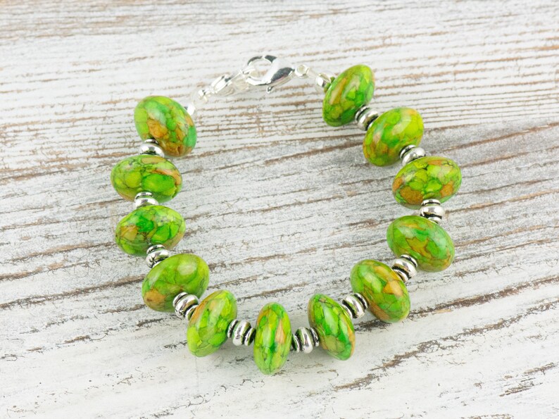 Pode incluir: Um bracelete de pedra verde e marrom com contas prateadas e um fecho prateado.