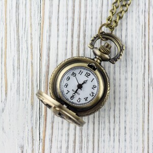 May include: A gold-toned pocket watch with a white face and black hands. The watch is on a chain and has a small, round case.