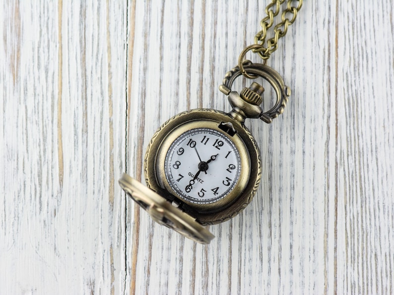 May include: A gold-toned pocket watch with a white face and black hands. The watch is on a chain and has a small, round case.