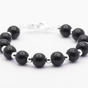 May include: A black beaded bracelet with silver accents. The bracelet is made of round, black beads and silver spacer beads. The clasp is a silver lobster claw.
