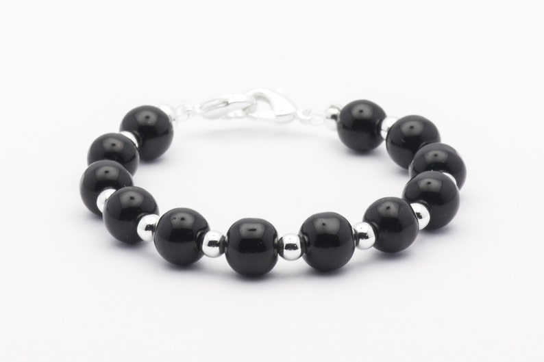 May include: A black beaded bracelet with silver accents. The bracelet is made of round, black beads and silver spacer beads. The clasp is a silver lobster claw.
