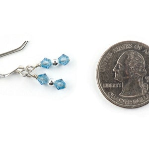 May include: A pair of silver earrings with light blue crystal beads. The earrings are shown next to a US quarter for size comparison.