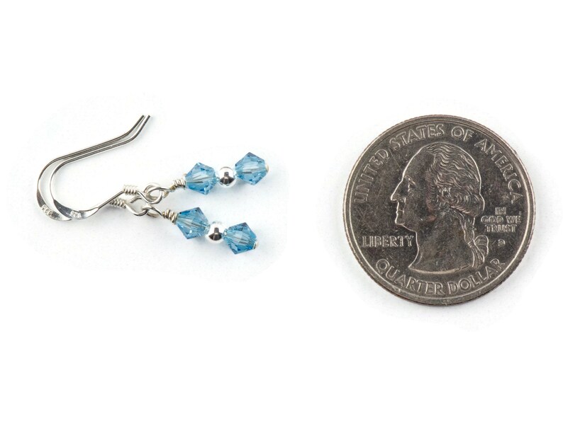 May include: A pair of silver earrings with light blue crystal beads. The earrings are shown next to a US quarter for size comparison.