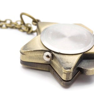 Peut inclure: Un collier avec un pendentif en forme d'&eacute;toile de couleur dor&eacute;e, avec un cadran de montre rond au dos. Le cadran de la montre est argent&eacute; et poss&egrave;de un petit bouton sur le c&ocirc;t&eacute;.
