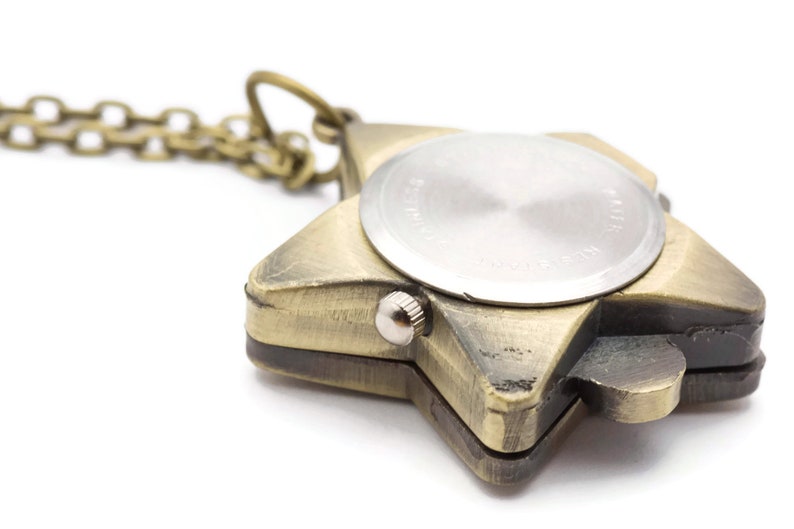 Peut inclure: Un collier avec un pendentif en forme d'&eacute;toile de couleur dor&eacute;e, avec un cadran de montre rond au dos. Le cadran de la montre est argent&eacute; et poss&egrave;de un petit bouton sur le c&ocirc;t&eacute;.
