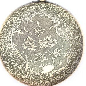 K&ouml;nnte beinhalten: Ein runder Anh&auml;nger aus Messing mit einem filigranen Blumenmuster. Das Design zeigt ein sich wiederholendes Muster aus Bl&auml;ttern und Spiralen.