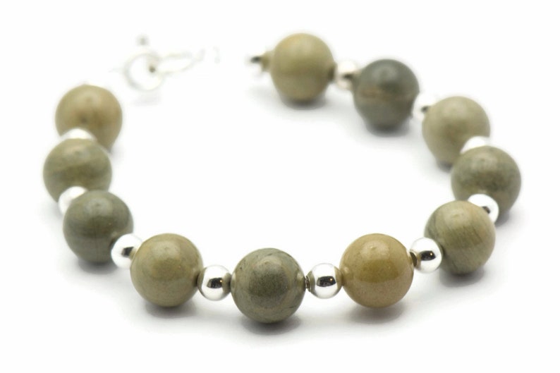 K&ouml;nnte beinhalten: Ein Armband aus gr&uuml;nen und braunen Steinperlen mit silbernen Akzenten. Das Armband besteht aus runden Perlen und hat ein schlichtes Design.
