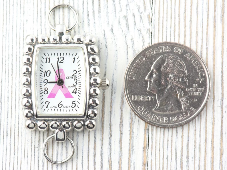 May include: Silver-toned watch with a rectangular face and a pink ribbon design. The watch face displays the time and the word "GENEVA". A U.S. quarter is next to the watch for size comparison.