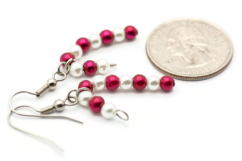 May include: A pair of earrings with alternating red and white beads. The earrings are made with small, round beads and have silver hooks.
