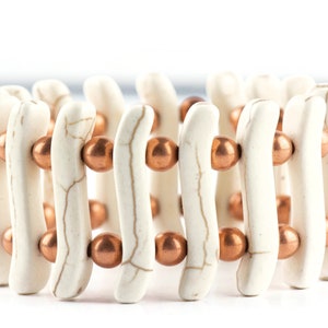May include: White and copper beaded bracelet with a wavy design. The bracelet is made of white beads with a marbled pattern and copper beads.