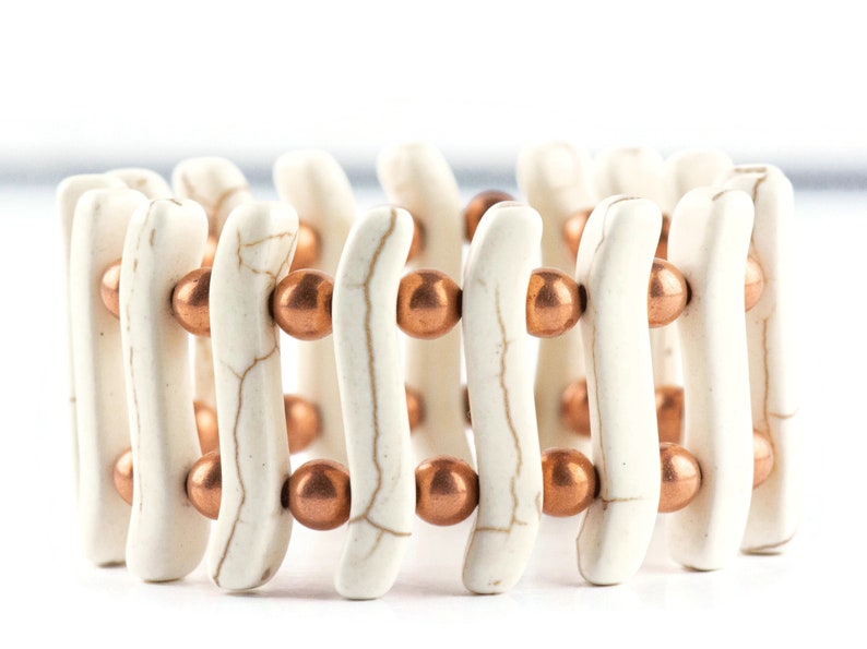 May include: White and copper beaded bracelet with a wavy design. The bracelet is made of white beads with a marbled pattern and copper beads.