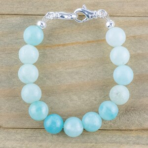 May include: A light blue gemstone bracelet with a silver clasp. The bracelet is made of round beads and is approximately 7 inches in length.