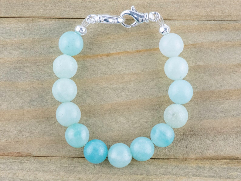 May include: A light blue gemstone bracelet with a silver clasp. The bracelet is made of round beads and is approximately 7 inches in length.