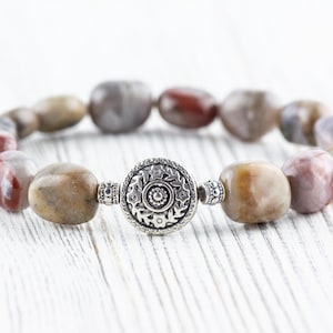 Op de afbeelding: Een armband gemaakt met bruine, witte en roze agaatstenen en een zilveren bedel met een bloemenmotief.