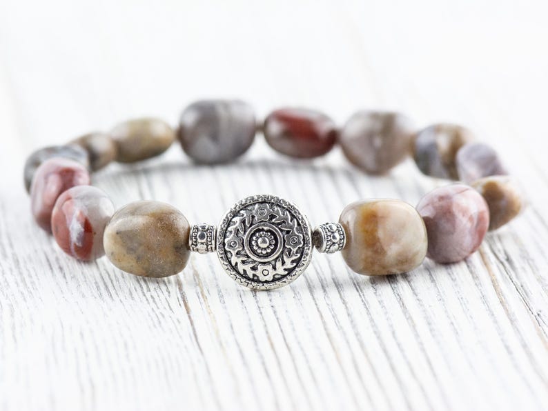 Op de afbeelding: Een armband gemaakt met bruine, witte en roze agaatstenen en een zilveren bedel met een bloemenmotief.