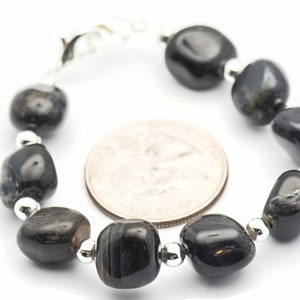 K&ouml;nnte beinhalten: Ein Armband aus schwarzen Edelsteinen mit silbernen Perlen. Das Armband ist etwa so gro&szlig; wie eine US-amerikanische 25-Cent-M&uuml;nze.