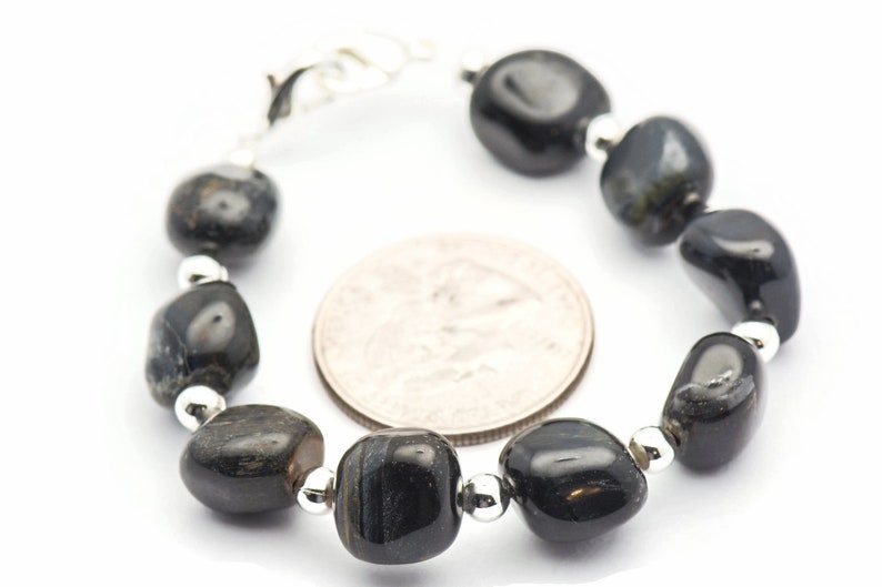 K&ouml;nnte beinhalten: Ein Armband aus schwarzen Edelsteinen mit silbernen Perlen. Das Armband ist etwa so gro&szlig; wie eine US-amerikanische 25-Cent-M&uuml;nze.