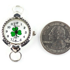 Peut inclure: Une montre argent&eacute;e avec un cadran blanc et un tr&egrave;fle vert. La montre est &agrave; peu pr&egrave;s de la taille d'une pi&egrave;ce de 25 cents am&eacute;ricaine.