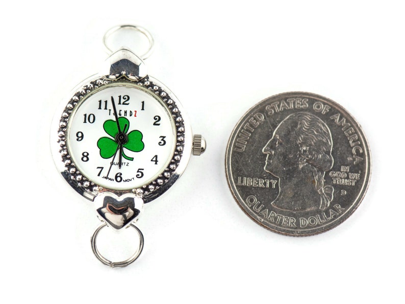 Peut inclure: Une montre argent&eacute;e avec un cadran blanc et un tr&egrave;fle vert. La montre est &agrave; peu pr&egrave;s de la taille d'une pi&egrave;ce de 25 cents am&eacute;ricaine.