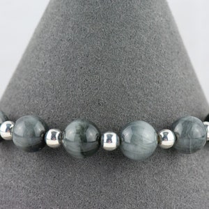May include: A gray and silver beaded bracelet with round beads. The beads have a striated pattern.