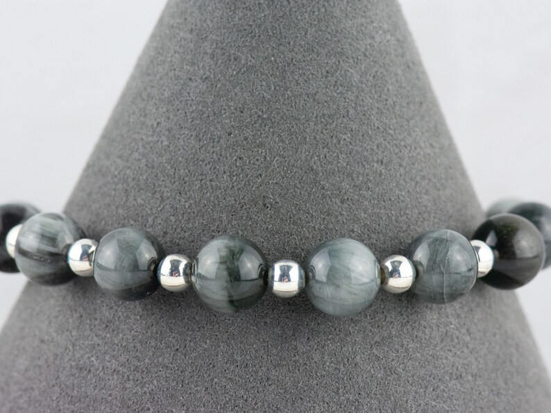 May include: A gray and silver beaded bracelet with round beads. The beads have a striated pattern.
