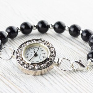 Pu&ograve; includere: Bracciale orologio al quarzo Geneva con quadrante argentato, quadrante bianco e dettagli in cristallo. Il bracciale &egrave; composto da grandi perle nere lucide ed elementi di collegamento argentati.
