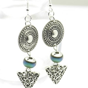 May include: Silver earrings with a round, ornate charm, a blue iridescent bead, and a triangular charm with a filigree design.