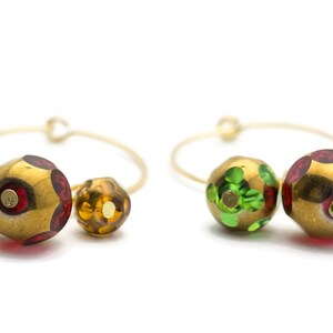May include: A pair of gold hoop earrings with three colorful glass beads. The beads are green, red, and gold with a speckled pattern.
