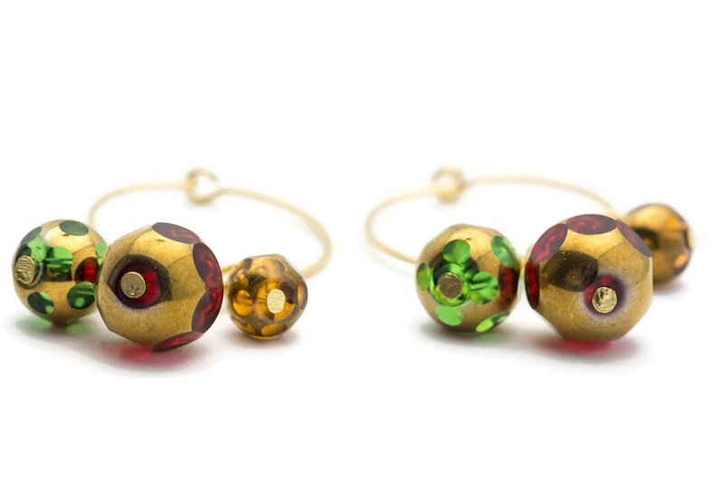 May include: A pair of gold hoop earrings with three colorful glass beads. The beads are green, red, and gold with a speckled pattern.