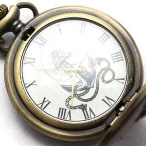 May include: A gold-toned pocket watch with a chain, featuring a white face with Roman numeral hour markers and an anchor design. The watch is open, revealing the inner workings.