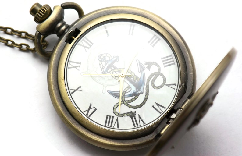 May include: A gold-toned pocket watch with a chain, featuring a white face with Roman numeral hour markers and an anchor design. The watch is open, revealing the inner workings.