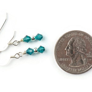 May include: A pair of silver earrings with teal blue crystal beads. The earrings are about the size of a US quarter.