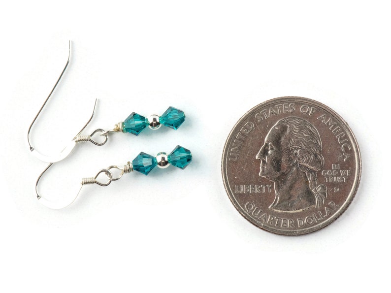 May include: A pair of silver earrings with teal blue crystal beads. The earrings are about the size of a US quarter.