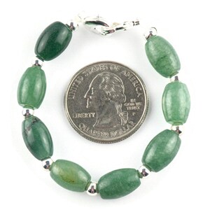 May include: A green jade stone bracelet with silver beads and a silver clasp. The bracelet is about the size of a US quarter.