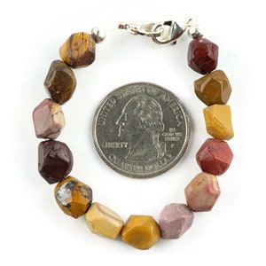 May include: A bracelet made with multi-colored, faceted, gemstone beads. The beads are a mix of brown, red, and yellow. The bracelet is about the size of a US quarter.
