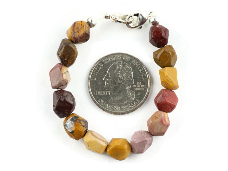 May include: A bracelet made with multi-colored, faceted, gemstone beads. The beads are a mix of brown, red, and yellow. The bracelet is about the size of a US quarter.