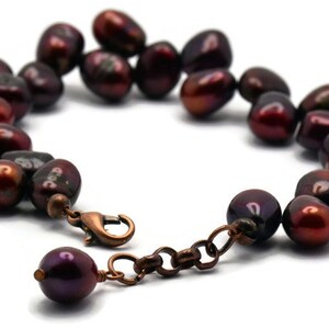 May include: A dark red freshwater pearl bracelet with a copper clasp. The pearls are irregular in shape and have a slightly iridescent sheen.