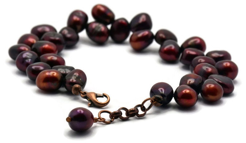 May include: A dark red freshwater pearl bracelet with a copper clasp. The pearls are irregular in shape and have a slightly iridescent sheen.