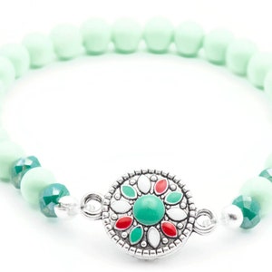 May include: A mint green beaded bracelet with a silver charm featuring a green, red and white floral design.