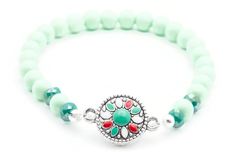 May include: A mint green beaded bracelet with a silver charm featuring a green, red and white floral design.