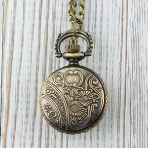 May include: A gold-toned pocket watch with a floral design on the face, hanging from a chain.