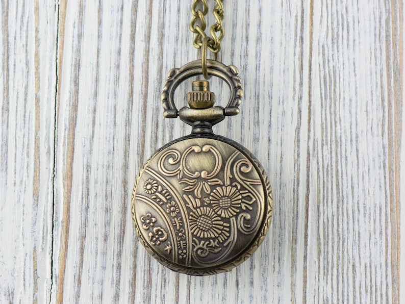 May include: A gold-toned pocket watch with a floral design on the face, hanging from a chain.