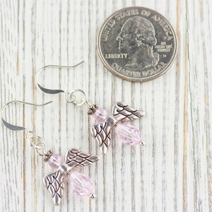 May include: A pair of silver angel wing earrings with pink crystal beads. The earrings are shown next to a US quarter for size comparison.