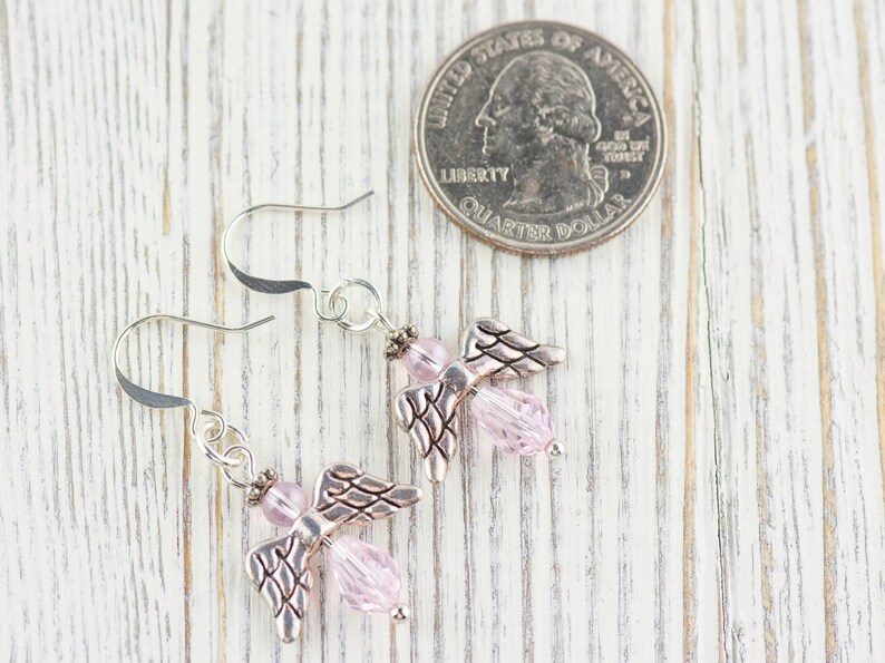 May include: A pair of silver angel wing earrings with pink crystal beads. The earrings are shown next to a US quarter for size comparison.