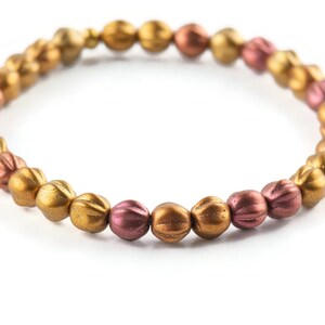 May include: A gold and copper beaded bracelet with a textured finish. The beads are round and have a slightly elongated shape.
