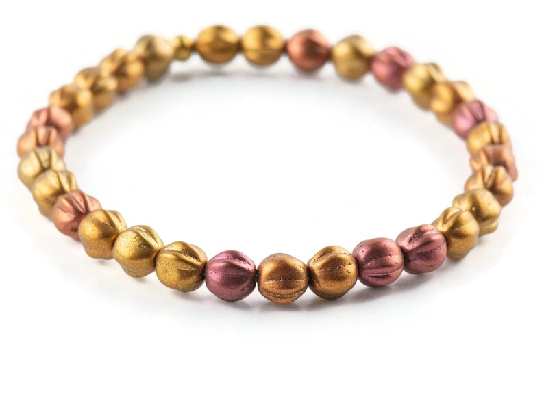 May include: A gold and copper beaded bracelet with a textured finish. The beads are round and have a slightly elongated shape.