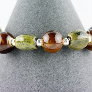 May include: A bracelet made of brown and green ceramic beads with silver spacers.